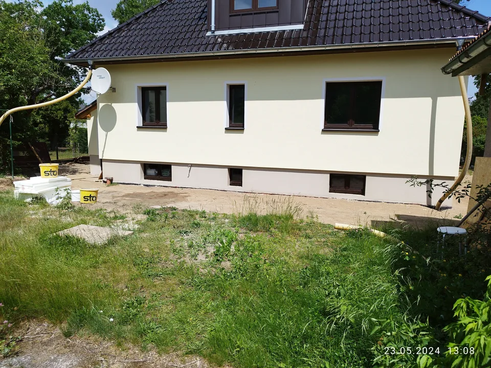 Hell verputzte Hausfassade mit dunklem Ziegeldach und abgesetztem Sockel