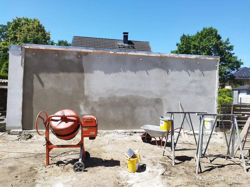 Außenwand während der Putzarbeiten mit Mörtelmischer und Arbeitsböcken