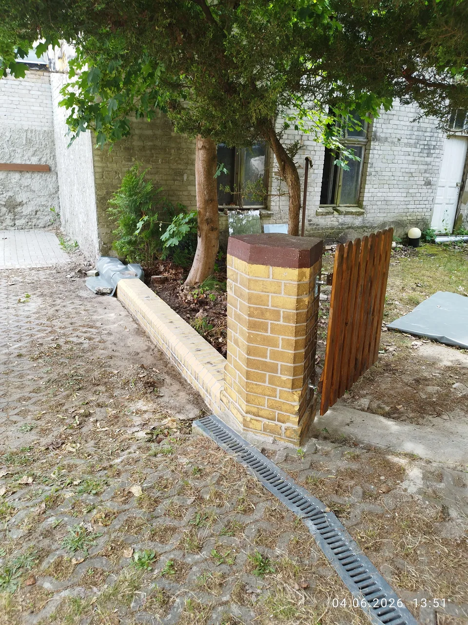Gemauerter gelber Torpfeiler neben einem hölzernen Gartentor