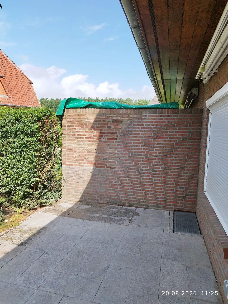 Neue rote Ziegelmauer zwischen Terrasse und Garten neben einem Wohnhaus